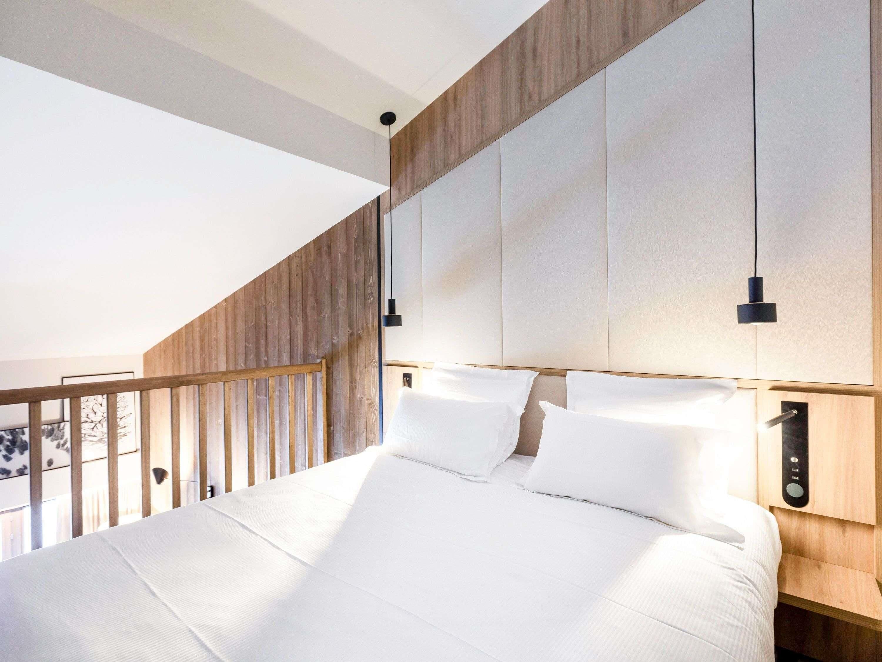 Een moderne slaapkamer met een schuine plafond, een houten hoofdbord en een bed met witte lakens.