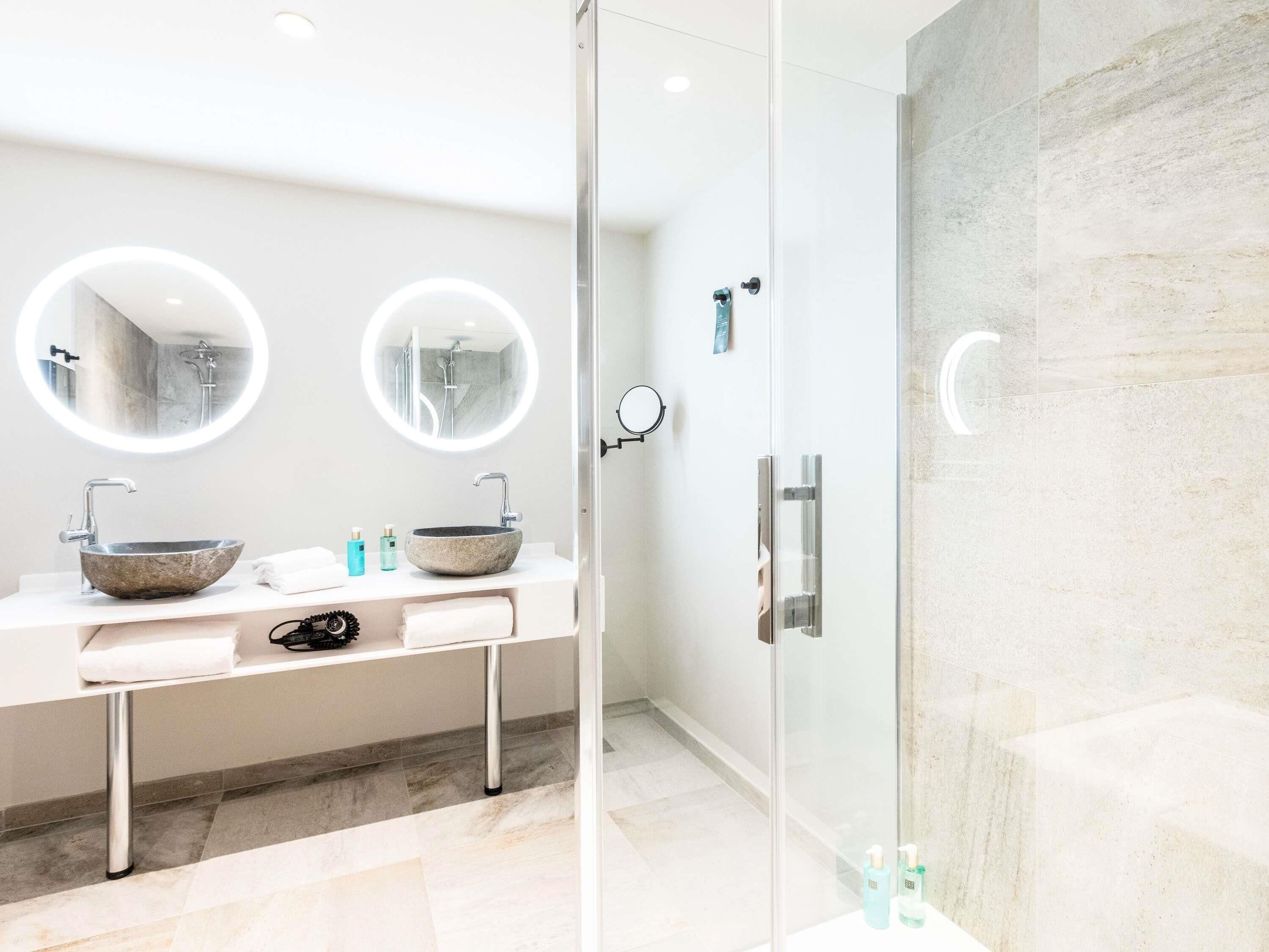 A modern bathroom with a glass-enclosed shower, two round mirrors, and a marble sink.
