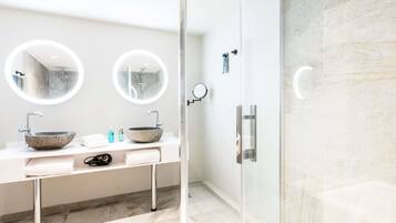 A modern bathroom with a glass-enclosed shower, two round mirrors, and a marble sink.