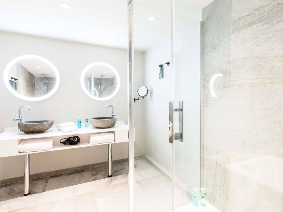 A modern bathroom with a glass-enclosed shower, two round mirrors, and a marble sink.