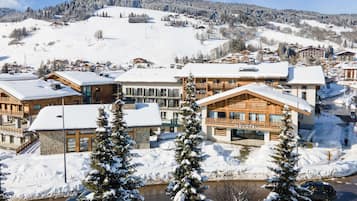 Un hôtel enneigé composé de plusieurs bâtiments, avec une rivière et un paysage montagneux en arrière-plan.