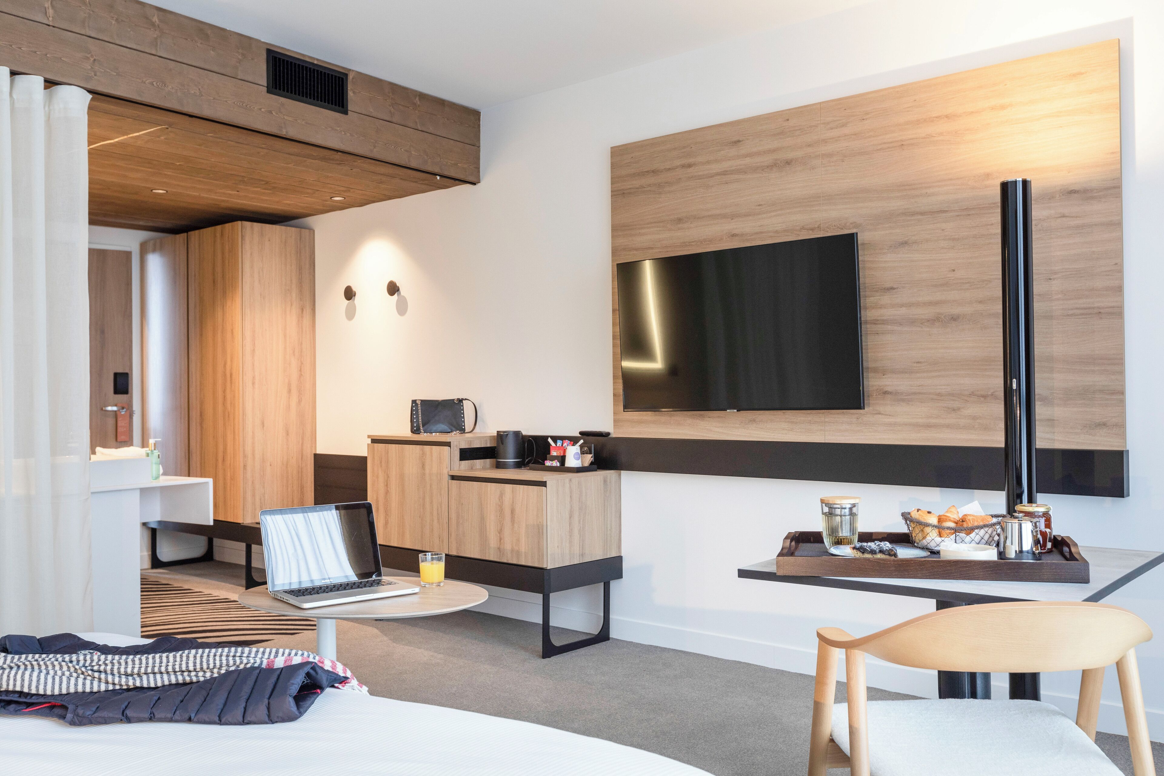 Una habitación de hotel moderna con una cama, un escritorio con una computadora portátil, un televisor de pantalla plana, una zona de café y un área de descanso.