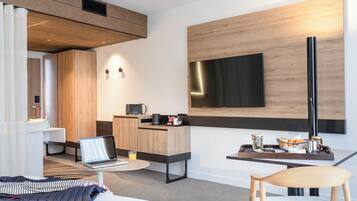 Una habitación de hotel moderna con una cama, un escritorio con una computadora portátil, un televisor de pantalla plana, una zona de café y un área de descanso.