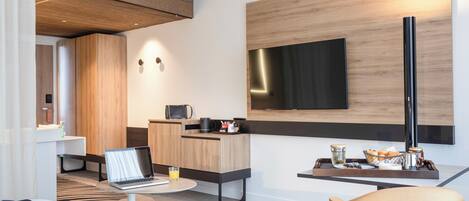 Una habitación de hotel moderna con una cama, un escritorio con una computadora portátil, un televisor de pantalla plana, una zona de café y un área de descanso.