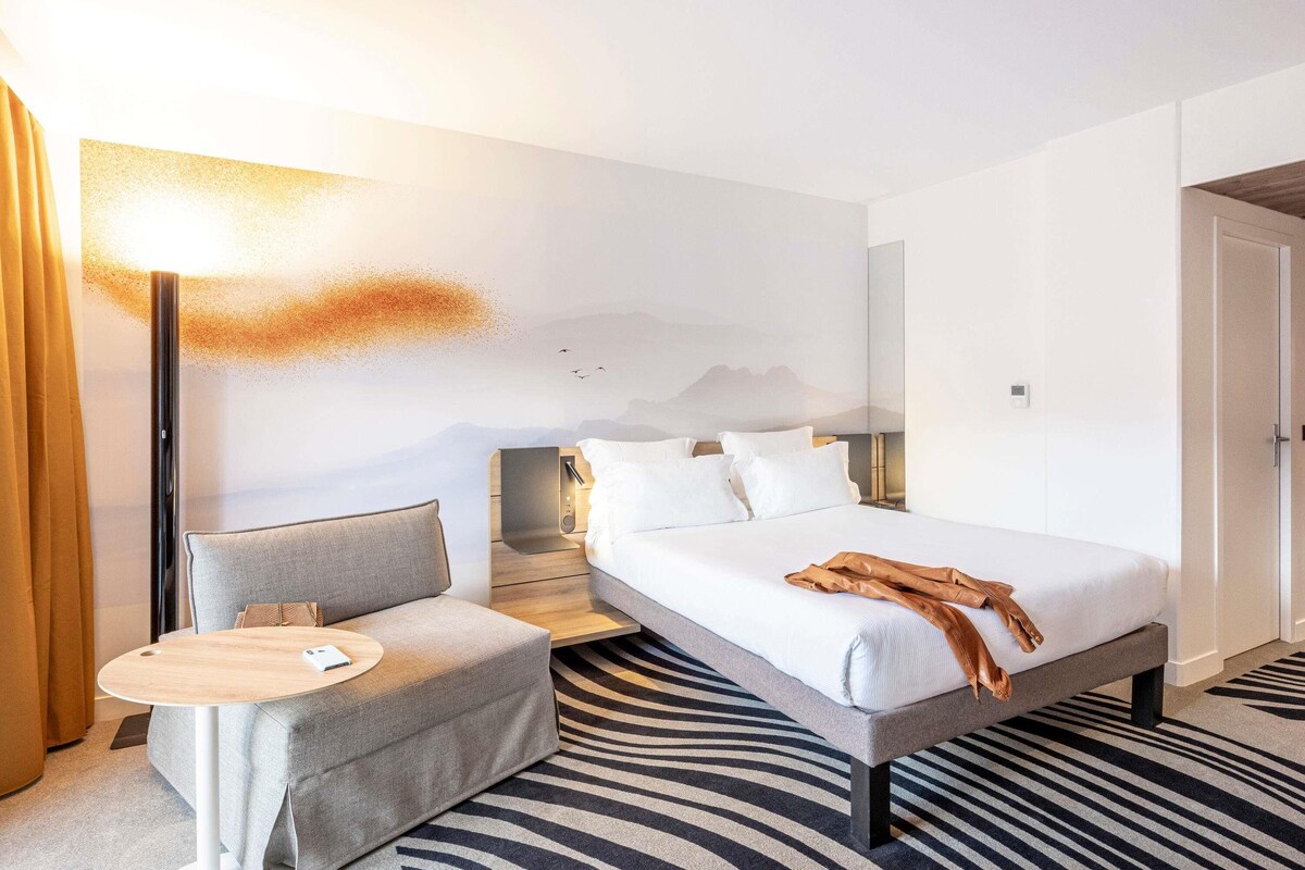 Une chambre d’hôtel avec un lit, un canapé, une petite table et une lampe fixée au mur.