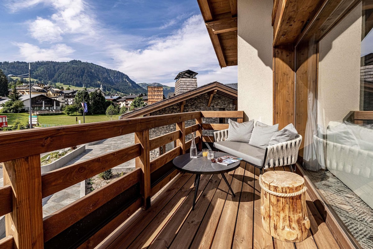 A wooden deck with a sofa and table, overlooking a mountainous landscape.