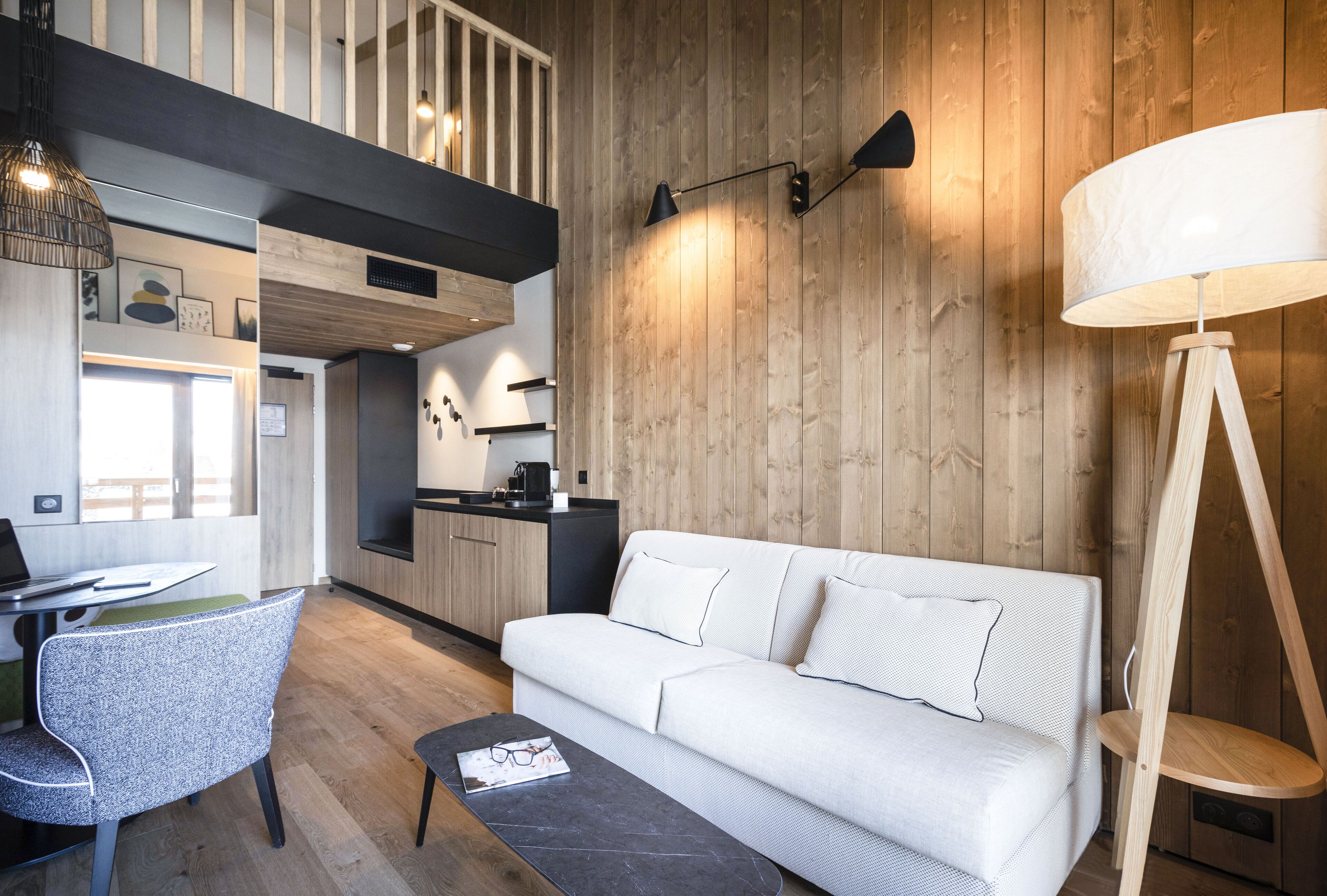 Een moderne woonkamer met een witte bank, een eethoek met een tafel en stoelen, een keuken op de achtergrond en een houten plafond.