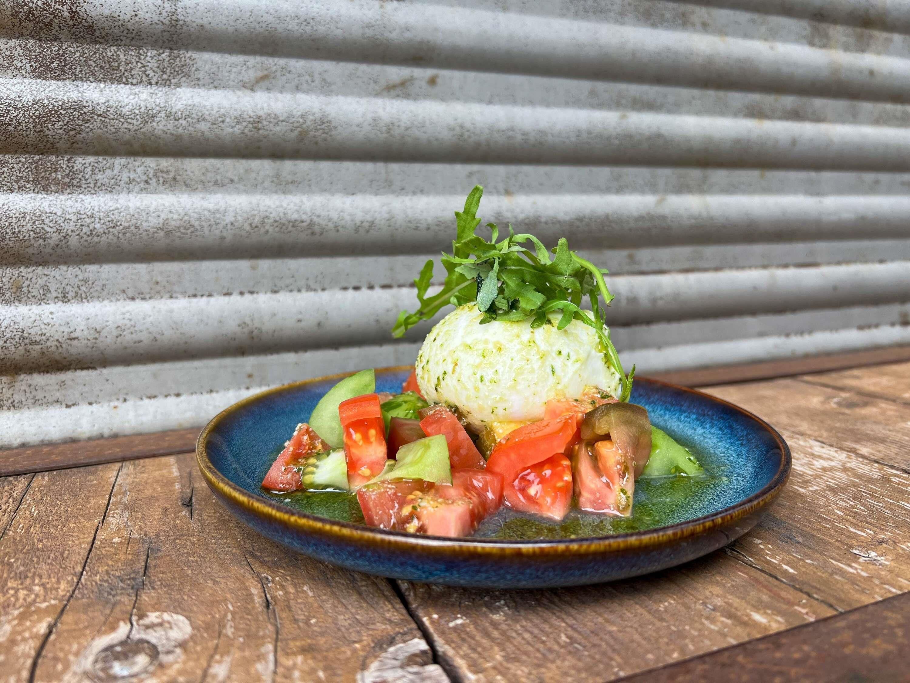 Une assiette en céramique bleue contenant un œuf poché, des légumes et une garniture.