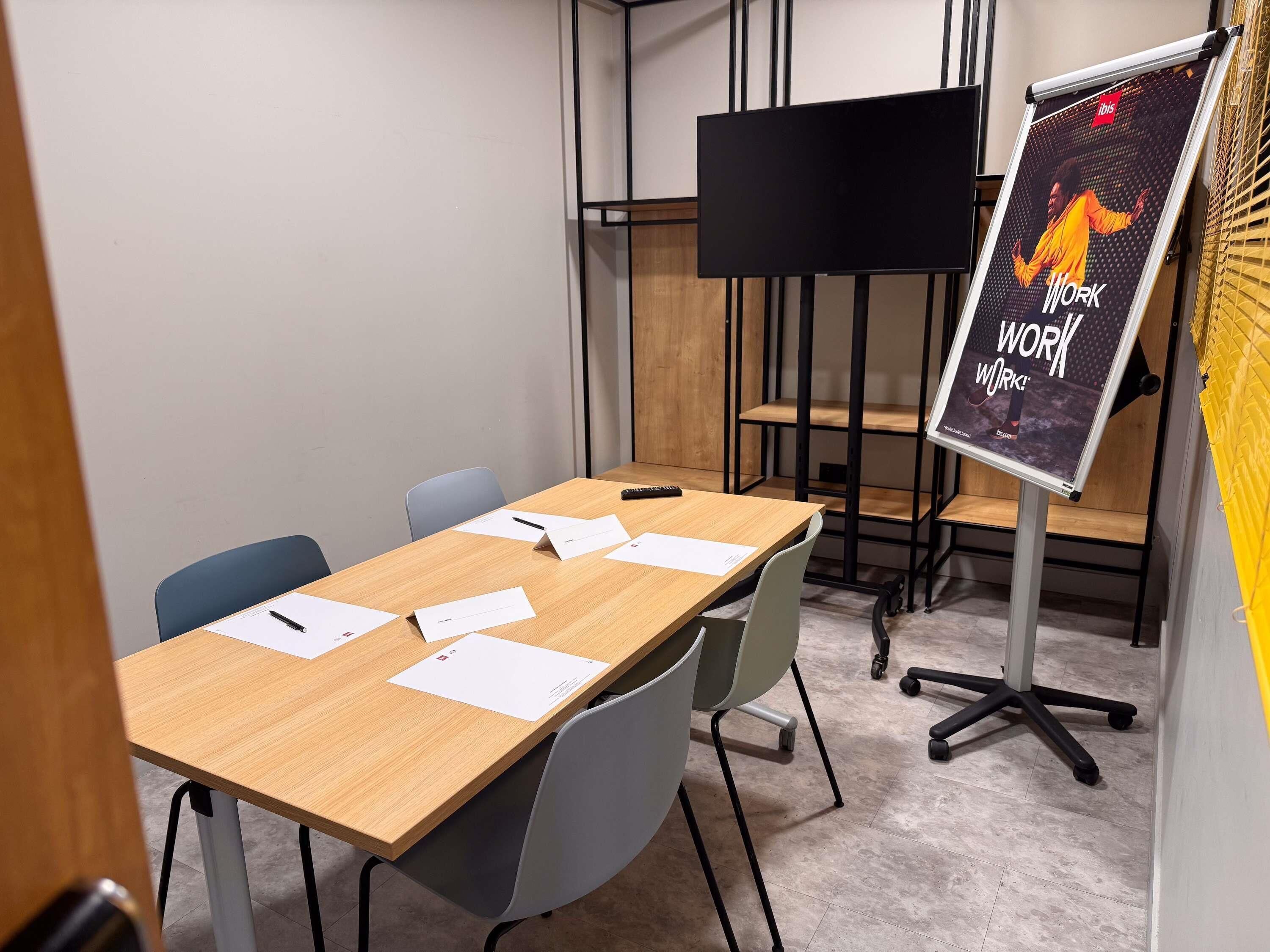 Ein Konferenzraum mit einem Holztisch, vier Stühlen, einem Flipchartständer mit einem Plakat und einem schwarzen Fernsehbildschirm.