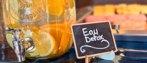 A beverage dispenser with a sign reading 'Eau Detox' and a glass filled with orange slices.