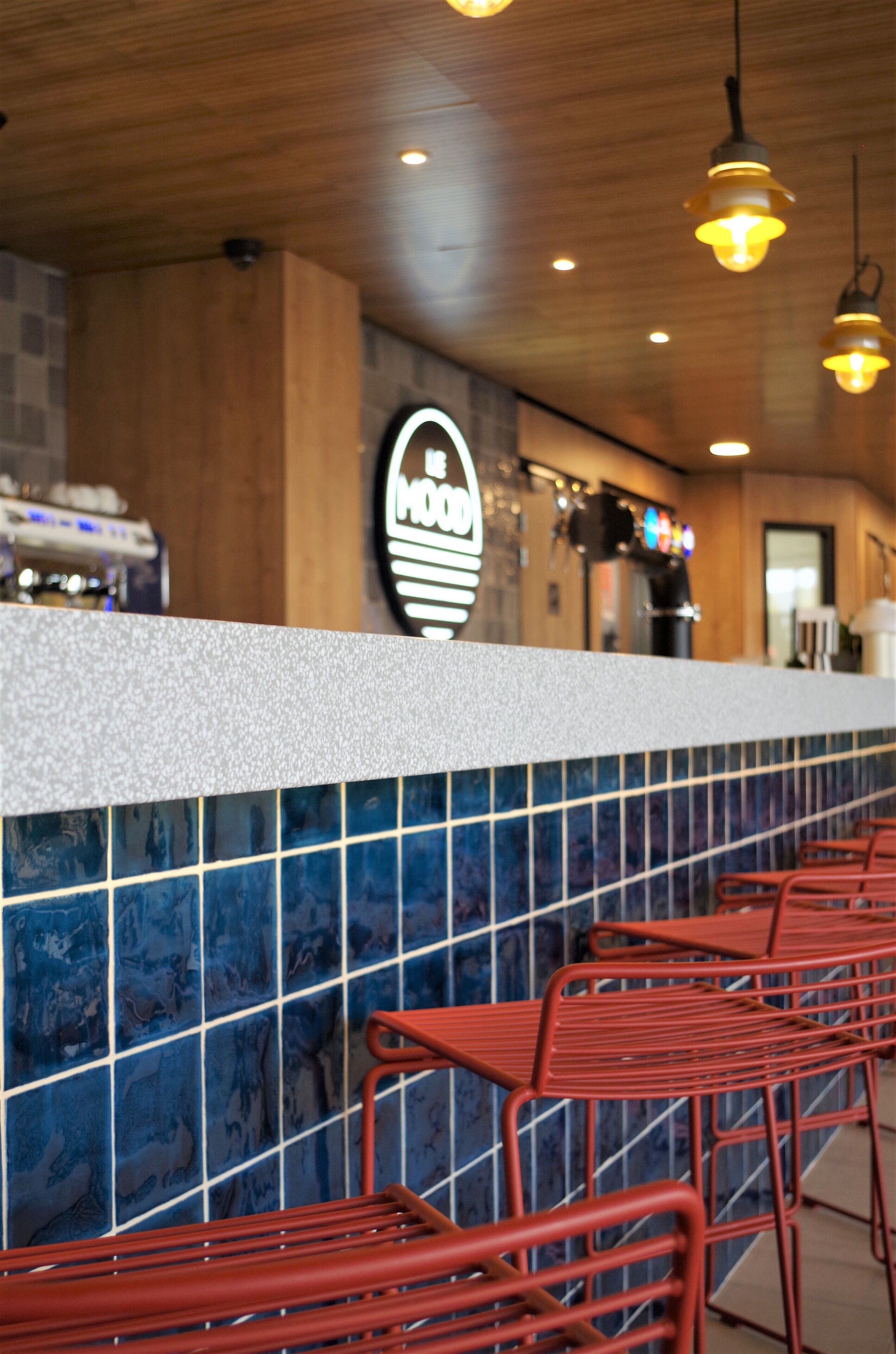 A bar area with a counter, blue-tiled backsplash, and red metal chairs.