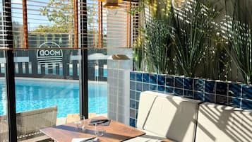 A poolside seating area with a table, chairs, and a view of a swimming pool.