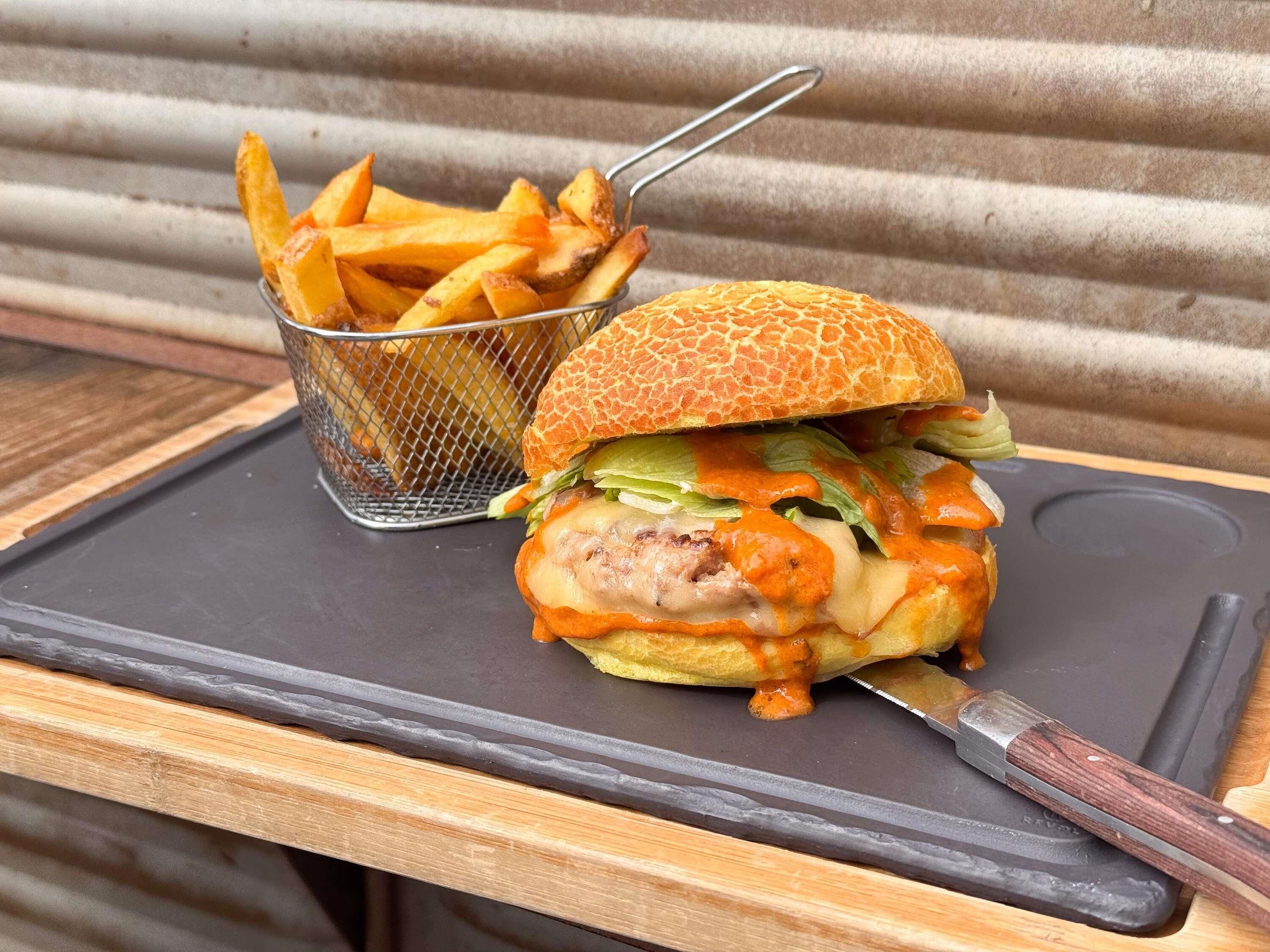 Un hamburger accompagné de frites, le tout servi sur un plateau noir.