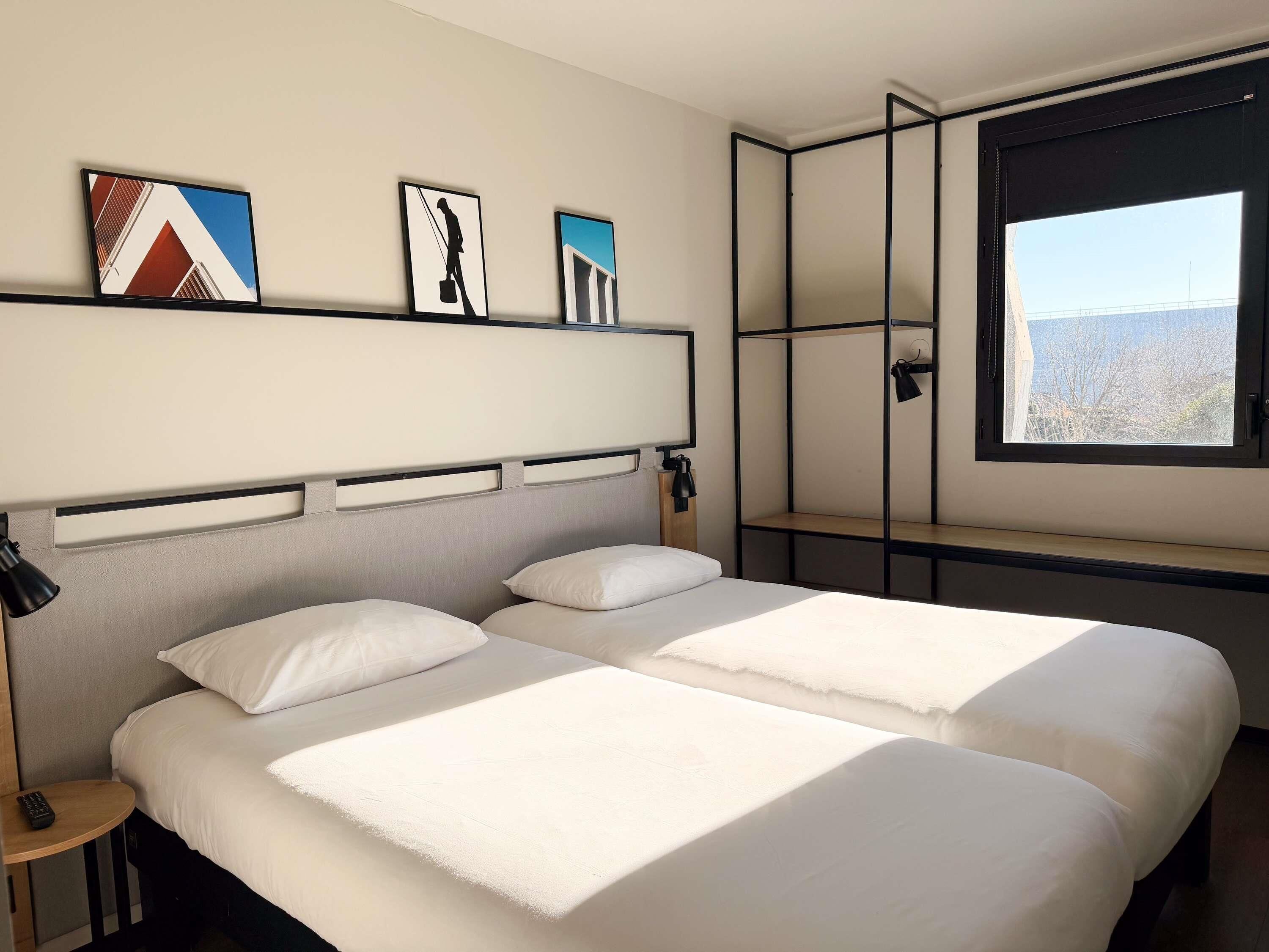 Ein Hotelzimmer mit zwei Betten, einem Fenster und Bildern an der Wand.