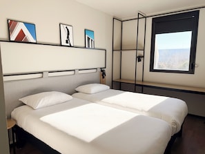 Ett hotellrum med två sängar, ett stort fönster och konstverk på väggen.