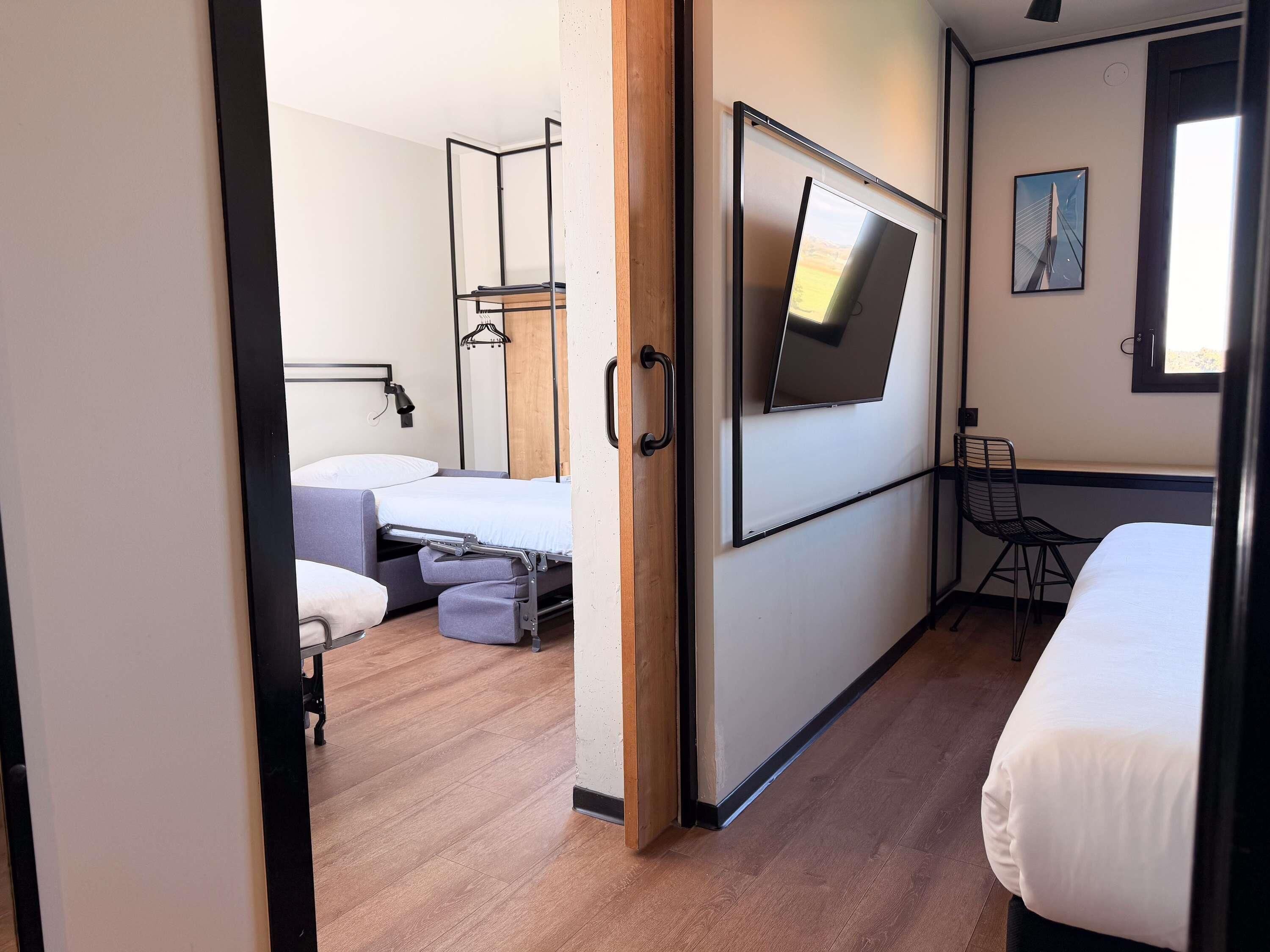 Een moderne hotelkamer met een bed, bureau, stoel en een aan de muur bevestigde televisie.
