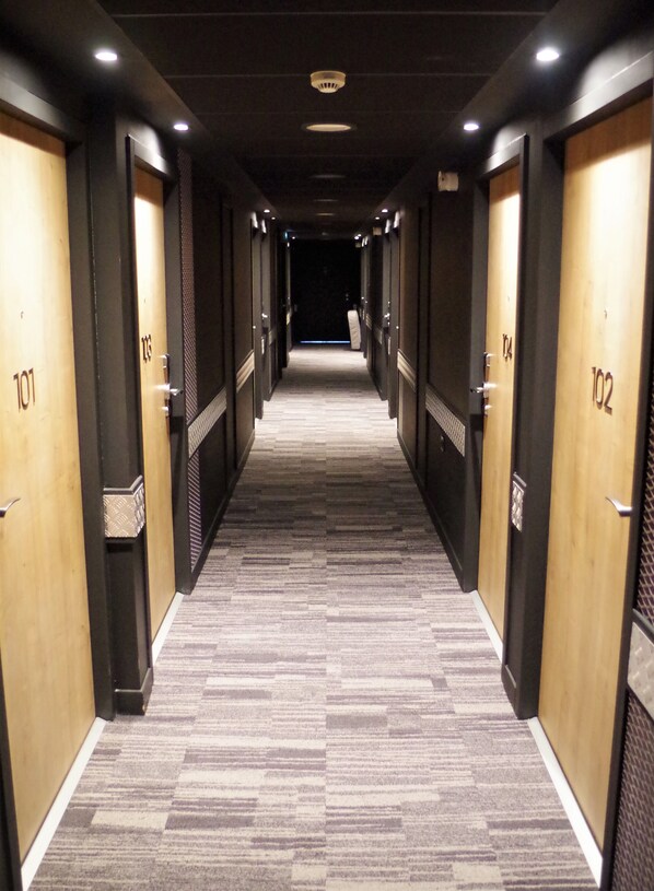 Pasillo de hotel con puertas numeradas del 101 al 102, suelo alfombrado e iluminación empotrada.