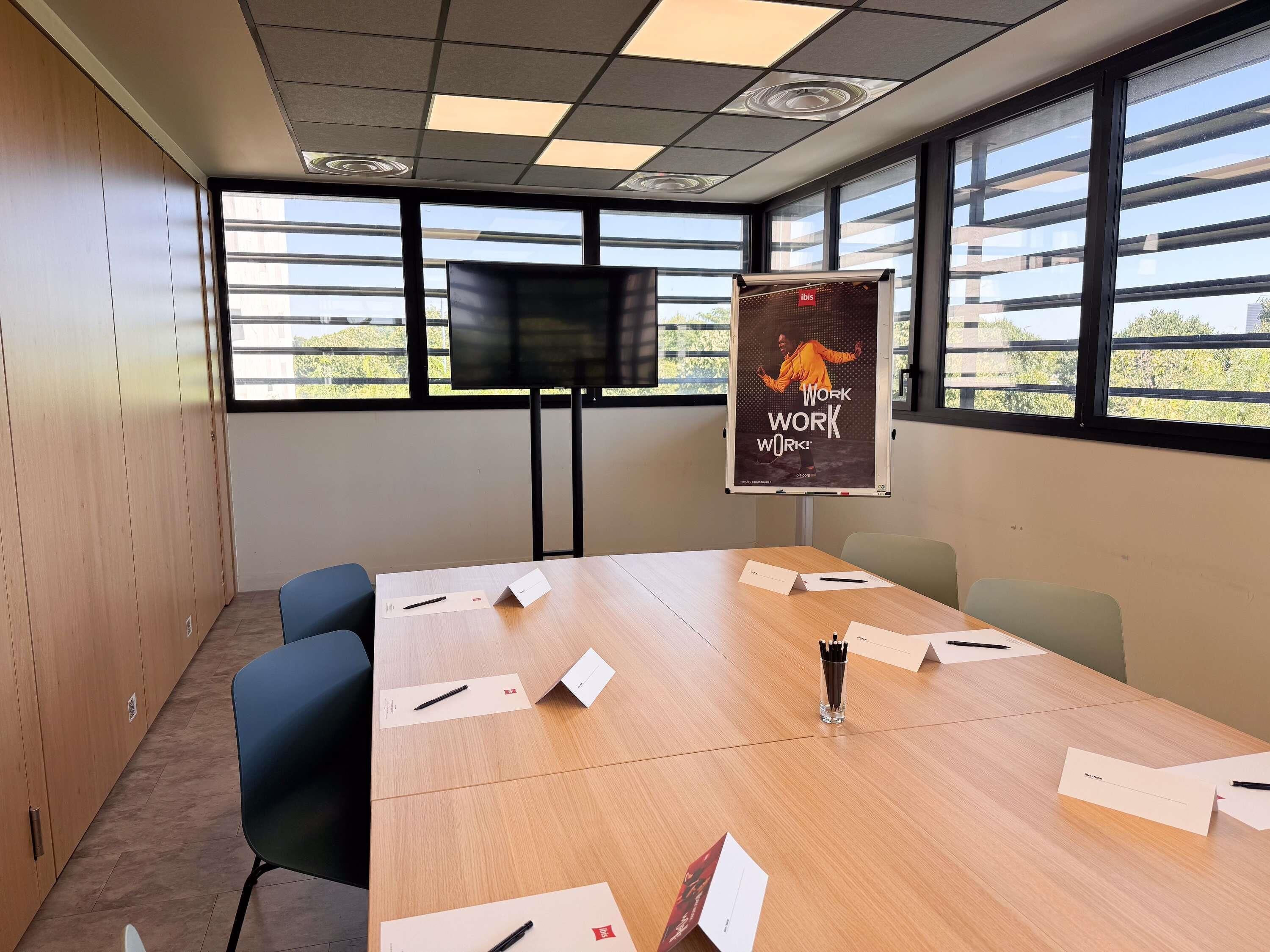A conference room with a long table, chairs, a projector screen, and a poster on the wall.