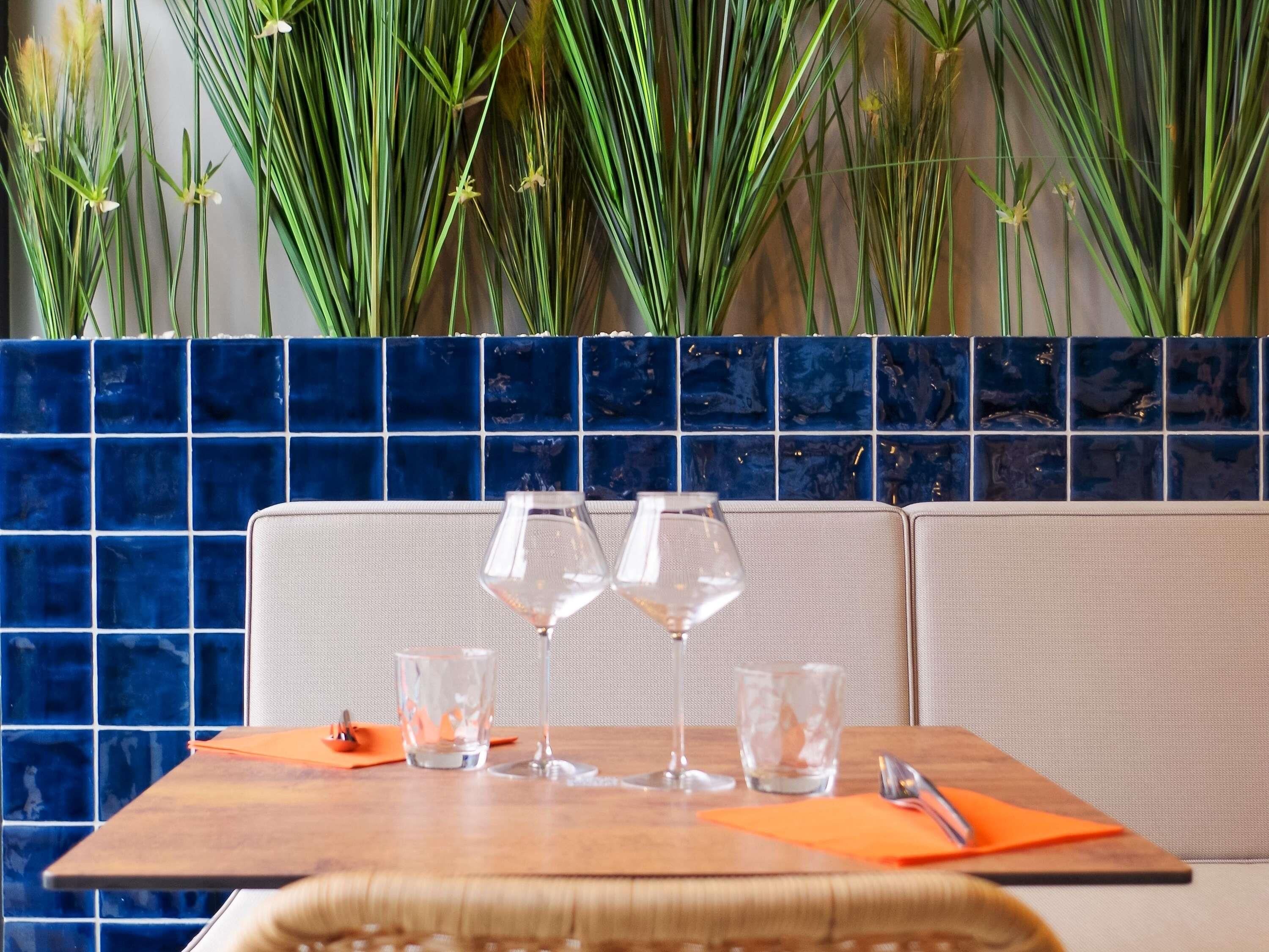 Una cabina ristorante con un rivestimento a mosaico blu, un tavolo di legno e due bicchieri da vino.
