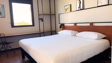 Una camera d'albergo con un letto grande, una finestra, una sedia e opere d'arte appese al muro.