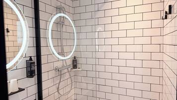 Une salle de bain moderne avec des carreaux de céramique blancs de type « métro », une douche en verre et un pommeau de douche à main.