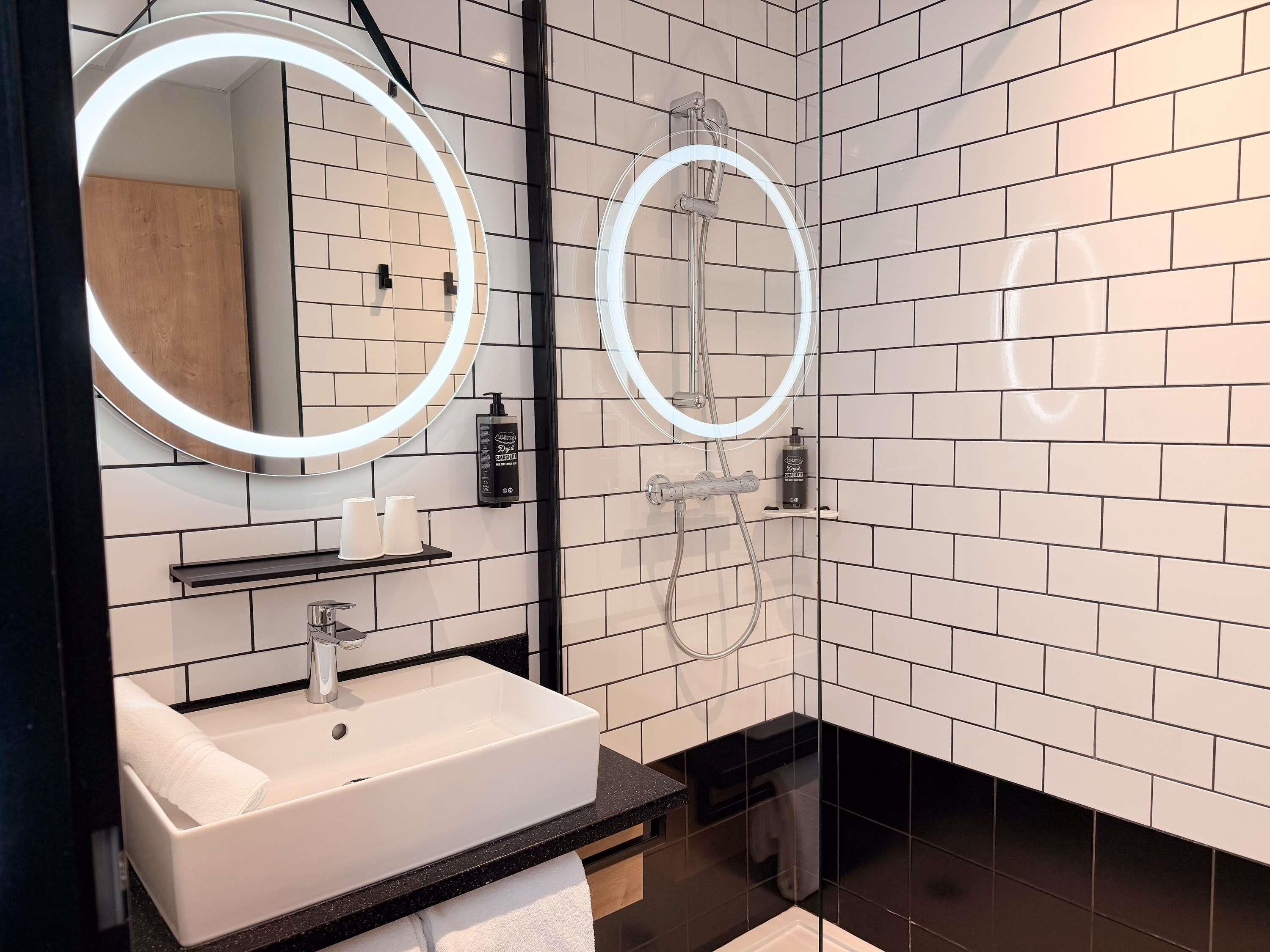 A modern bathroom with a white sink, a mirror, and a shower with a circular light.