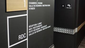 A hotel corridor with directional signs indicating meeting rooms, fitness area, and reception.