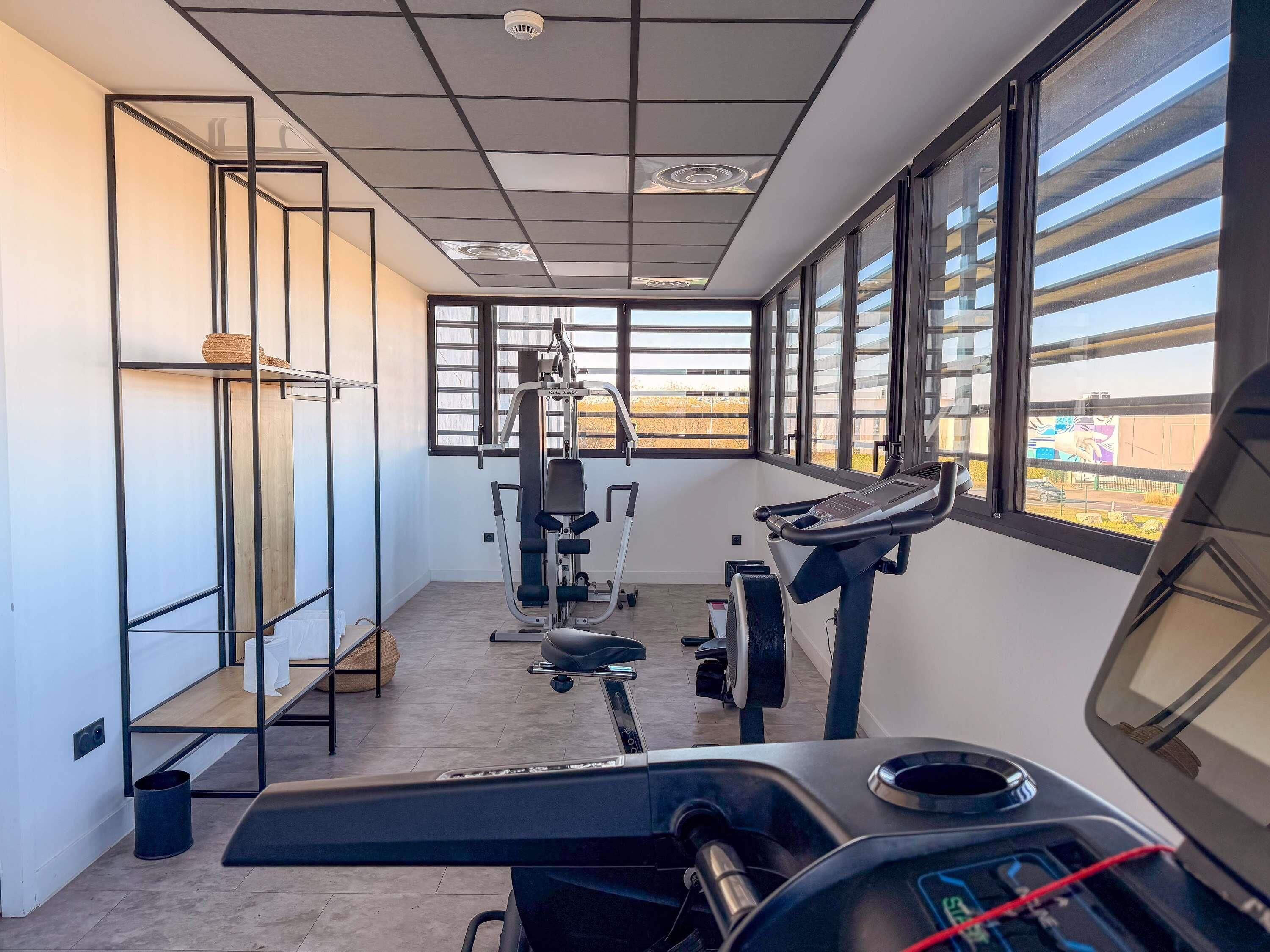 A gym with exercise equipment, large windows, and a view of the outside.