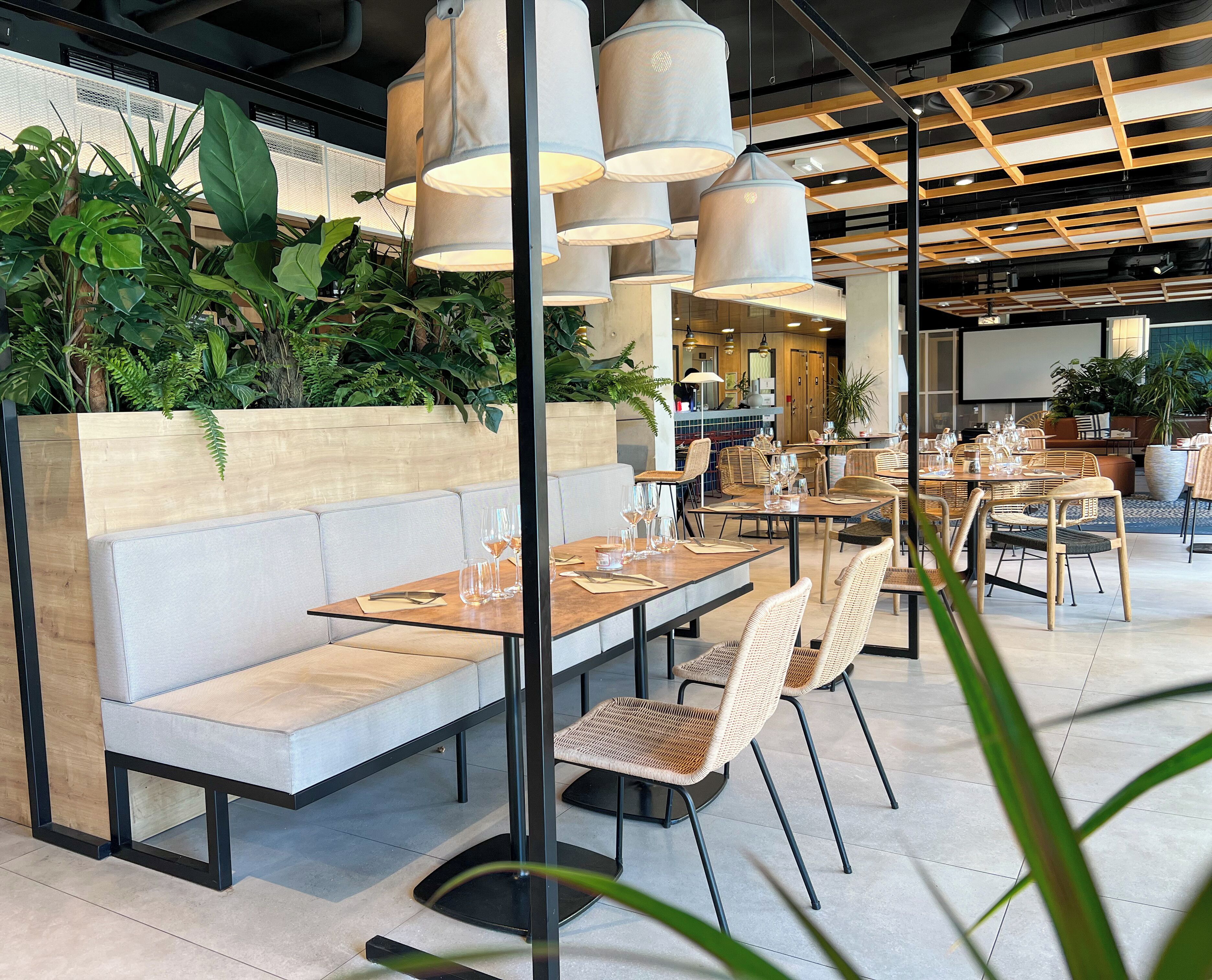 En moderne restaurant med træborde og polstrede siddepladser, omgivet af indeplanter.
