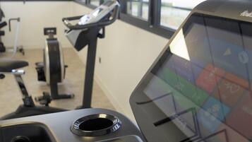 Ein Fitnessraum mit Trainingsgeräten, darunter ein Laufband und ein Ergometer, sowie ein Bildschirm.
