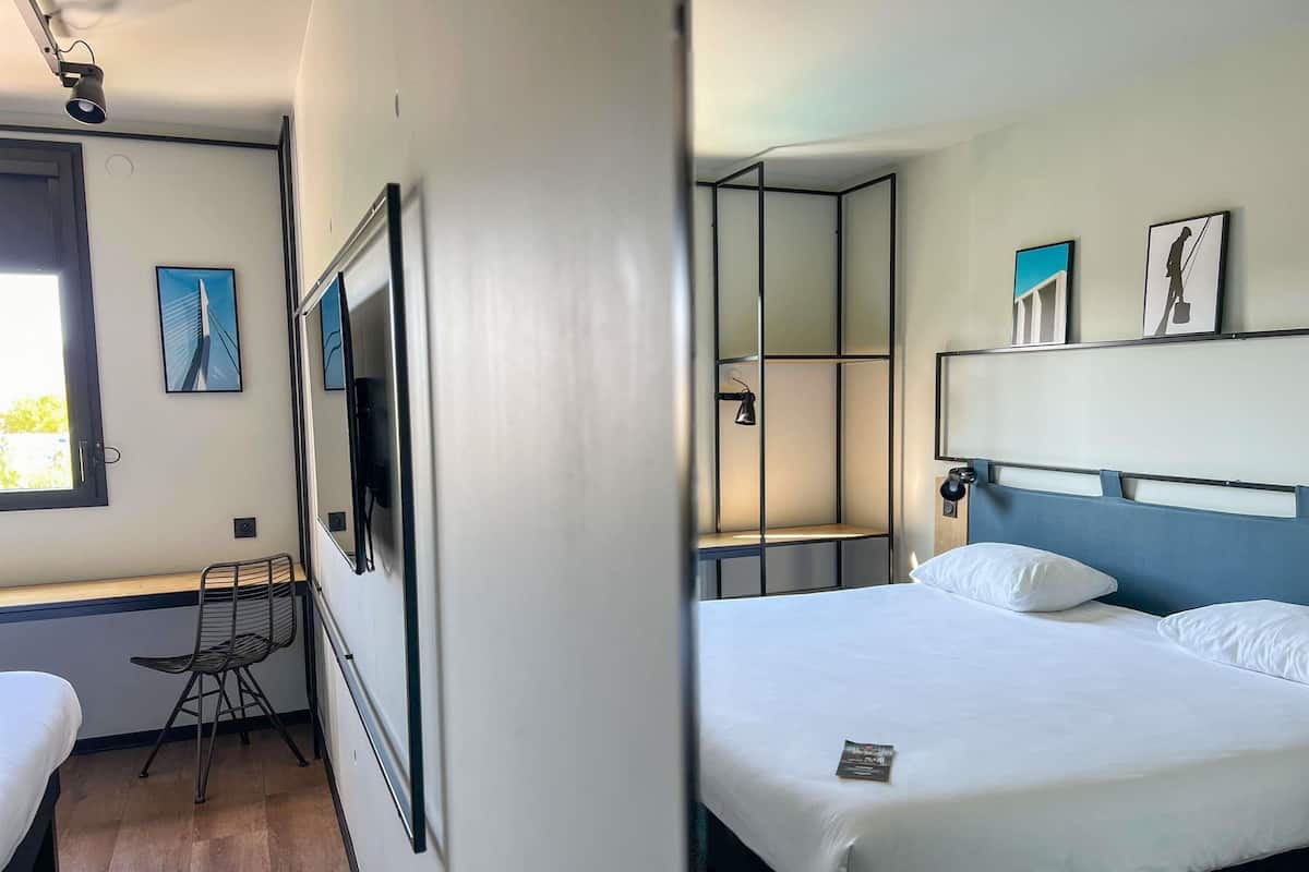 Ett modernt hotellrum med en säng, ett skrivbord och en stol. Det finns ett fönster med utsikt över en byggnad.