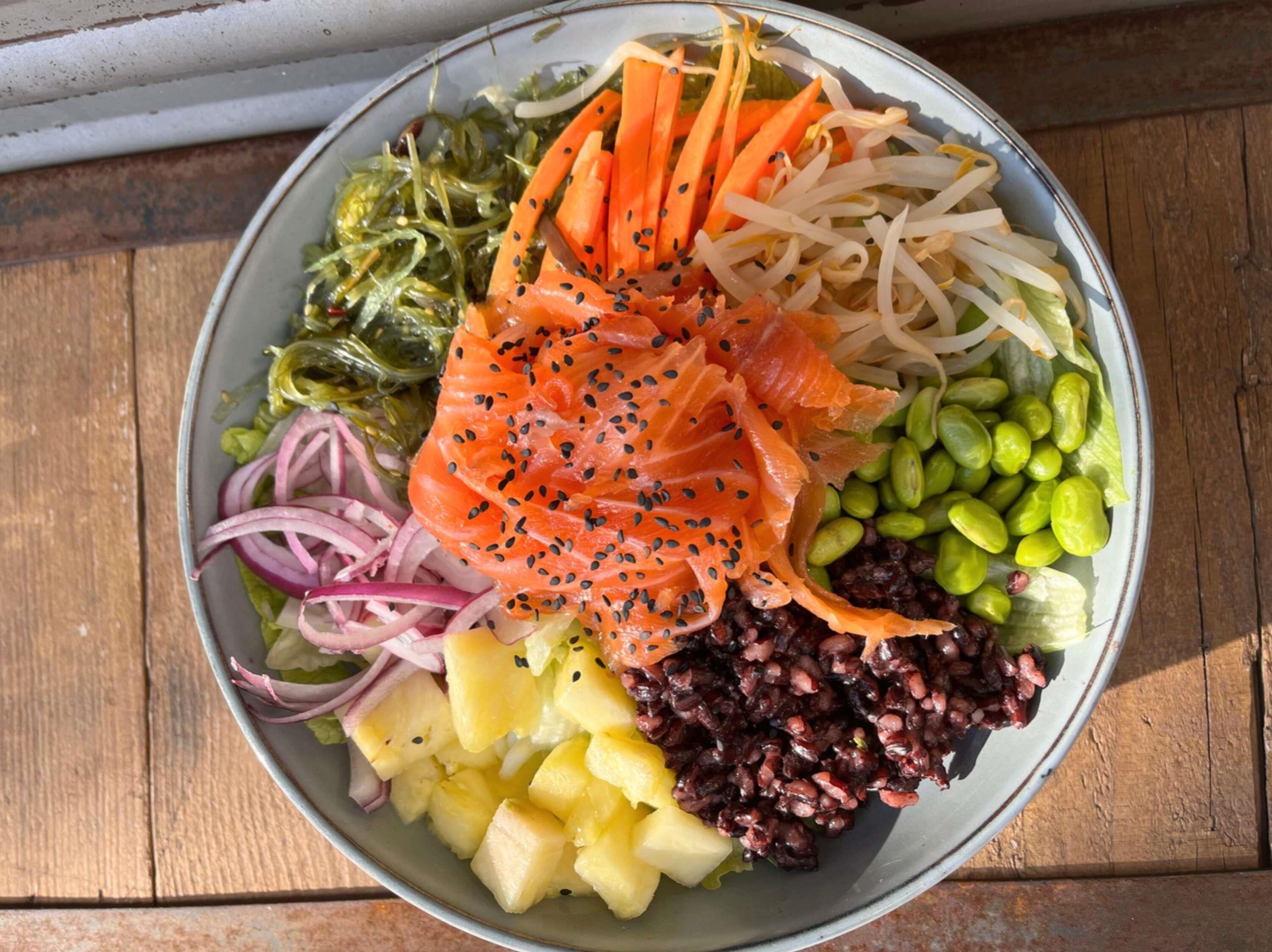 A bowl of assorted food including salmon, edamame, and red cabbage.