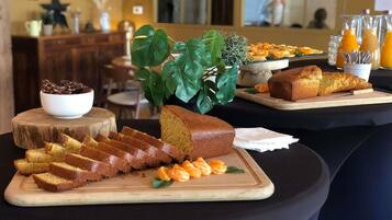 Ein Frühstücksbuffet mit verschiedenen Speisen, darunter Brot, Gebäck und einer Pflanzengesteck.
