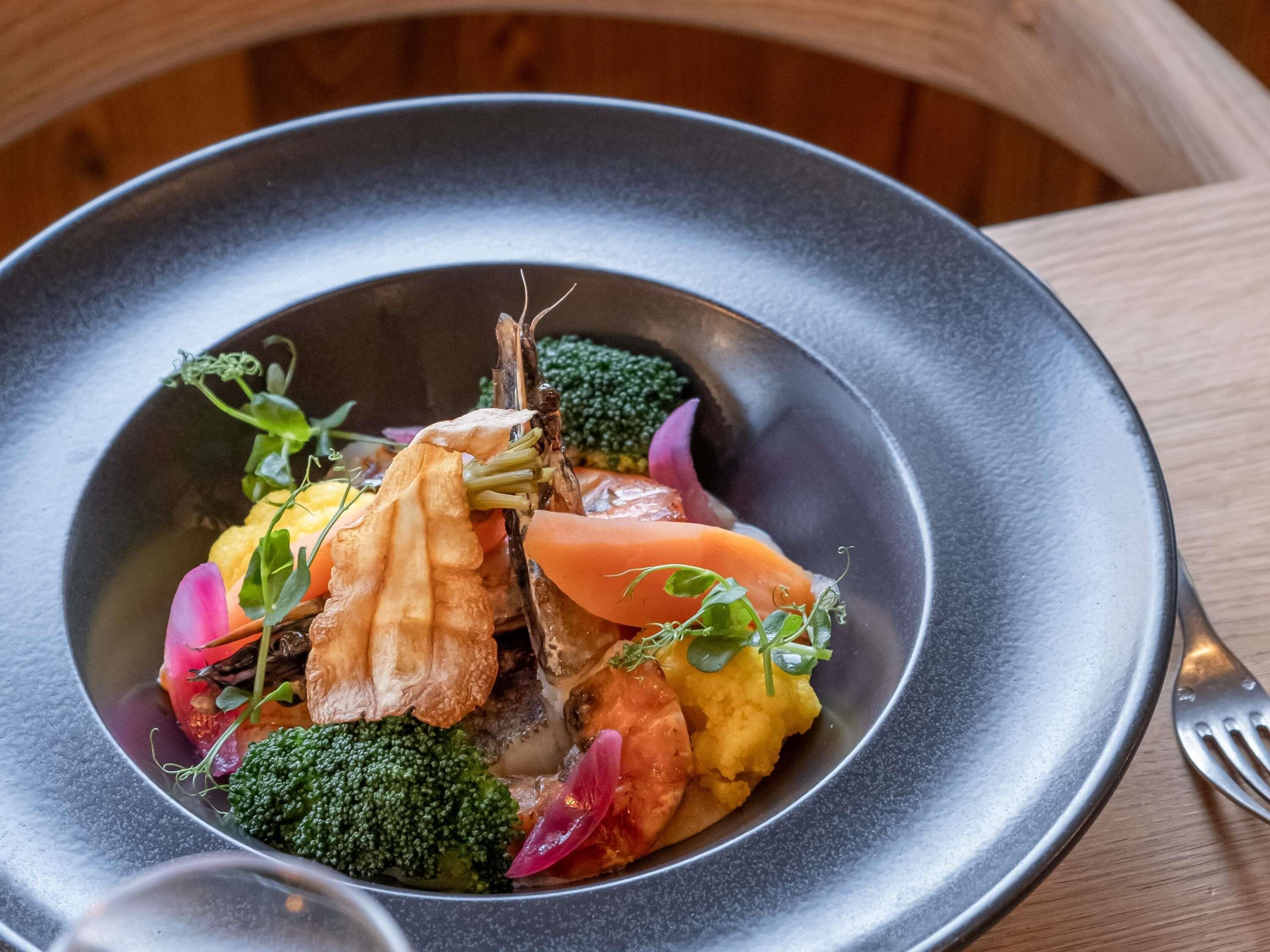 A plate of food with various vegetables and a piece of meat, served on a dark plate.