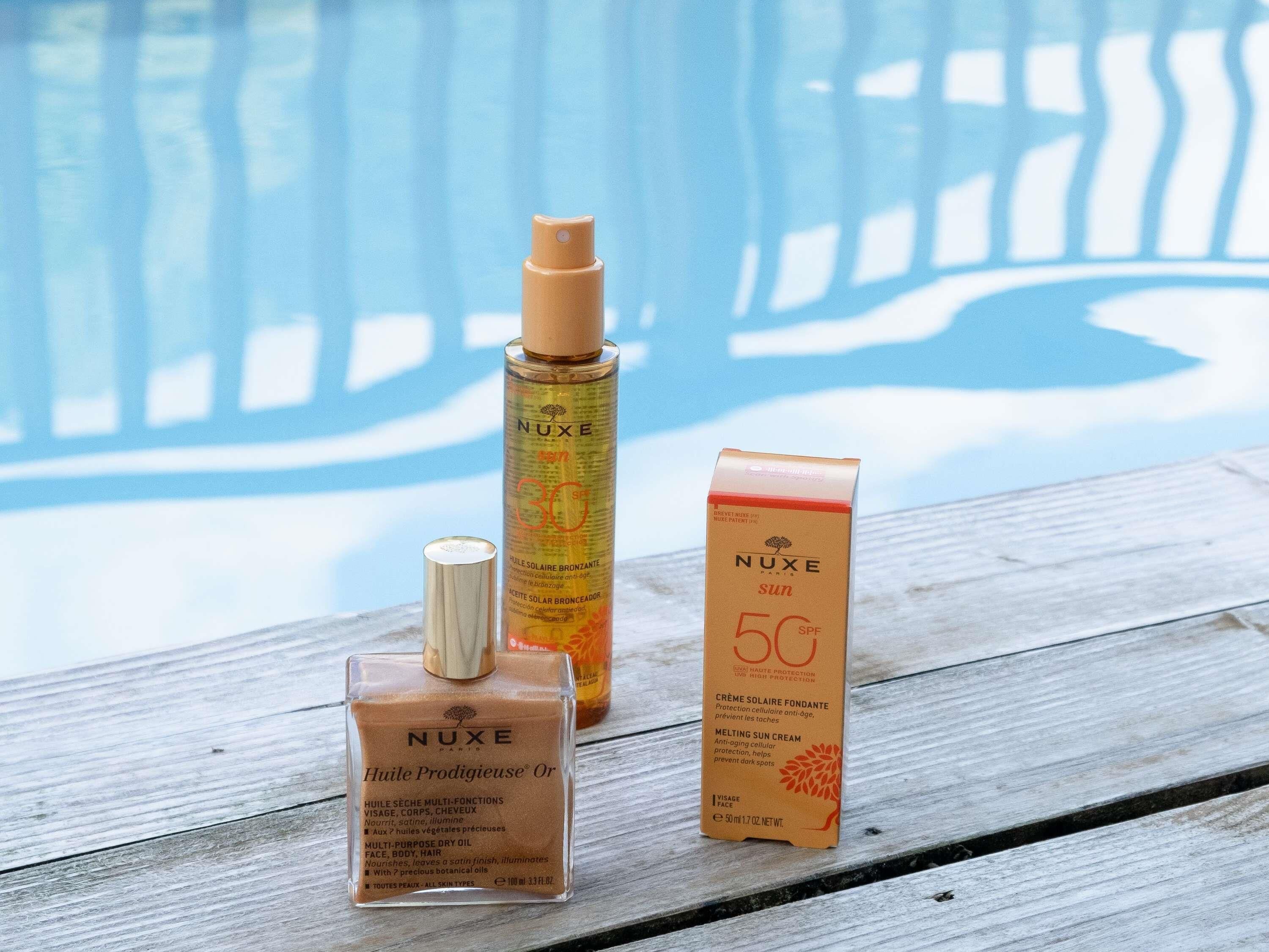 Tres productos de cuidado de la piel NUXE sobre una superficie de madera cerca de una piscina.