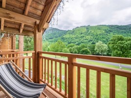 Una terraza de madera con una hamaca y vistas a un paisaje verde exuberante.