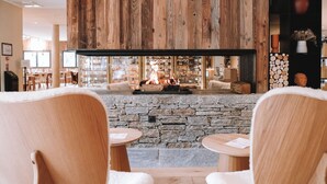 A cozy interior with a stone fireplace, wooden ceiling, and seating area with tables and chairs. - Hôtel Mercure Peyragudes Loudenvielle Pyrénées (Loudenvielle)