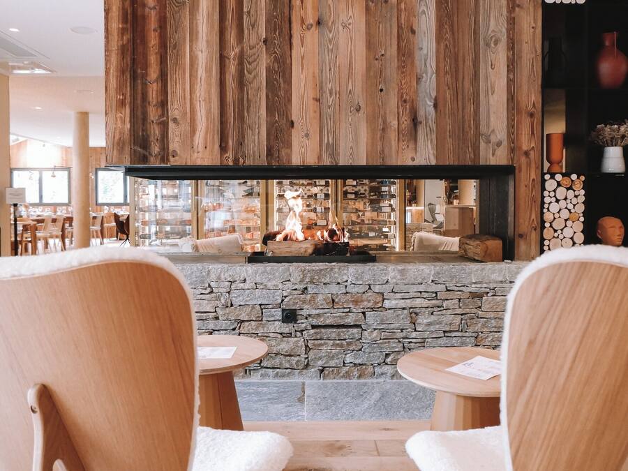 Un interior acogedor con chimenea de piedra, techo de madera y zona de estar con mesas y sillas.