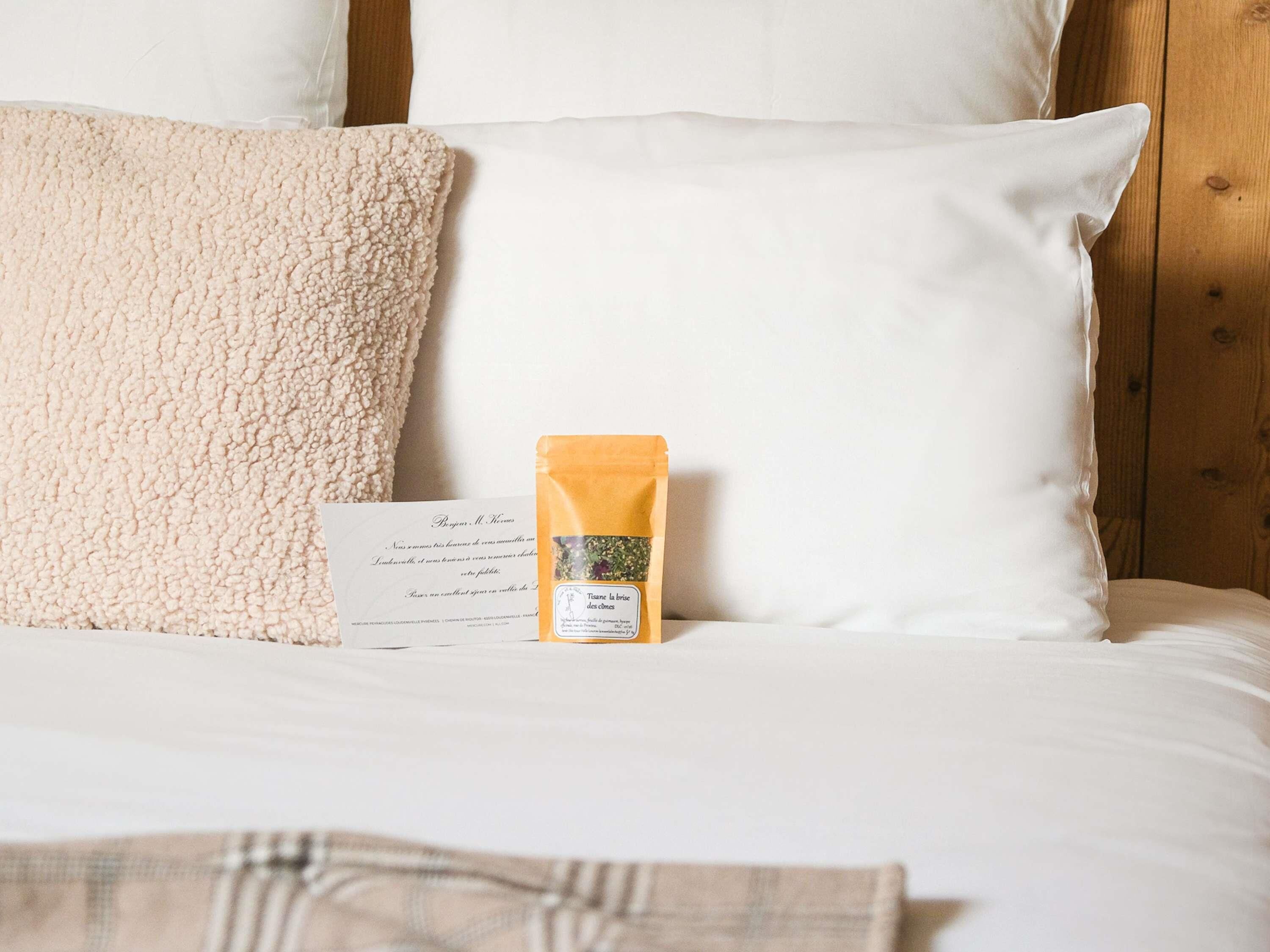 Una cama con almohadas blancas y una caja de té encima.