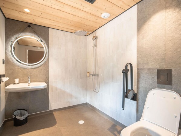 A modern bathroom with a wooden ceiling, a round mirror, a sink, a shower, and a toilet. - Hôtel Mercure Peyragudes Loudenvielle Pyrénées (Loudenvielle)