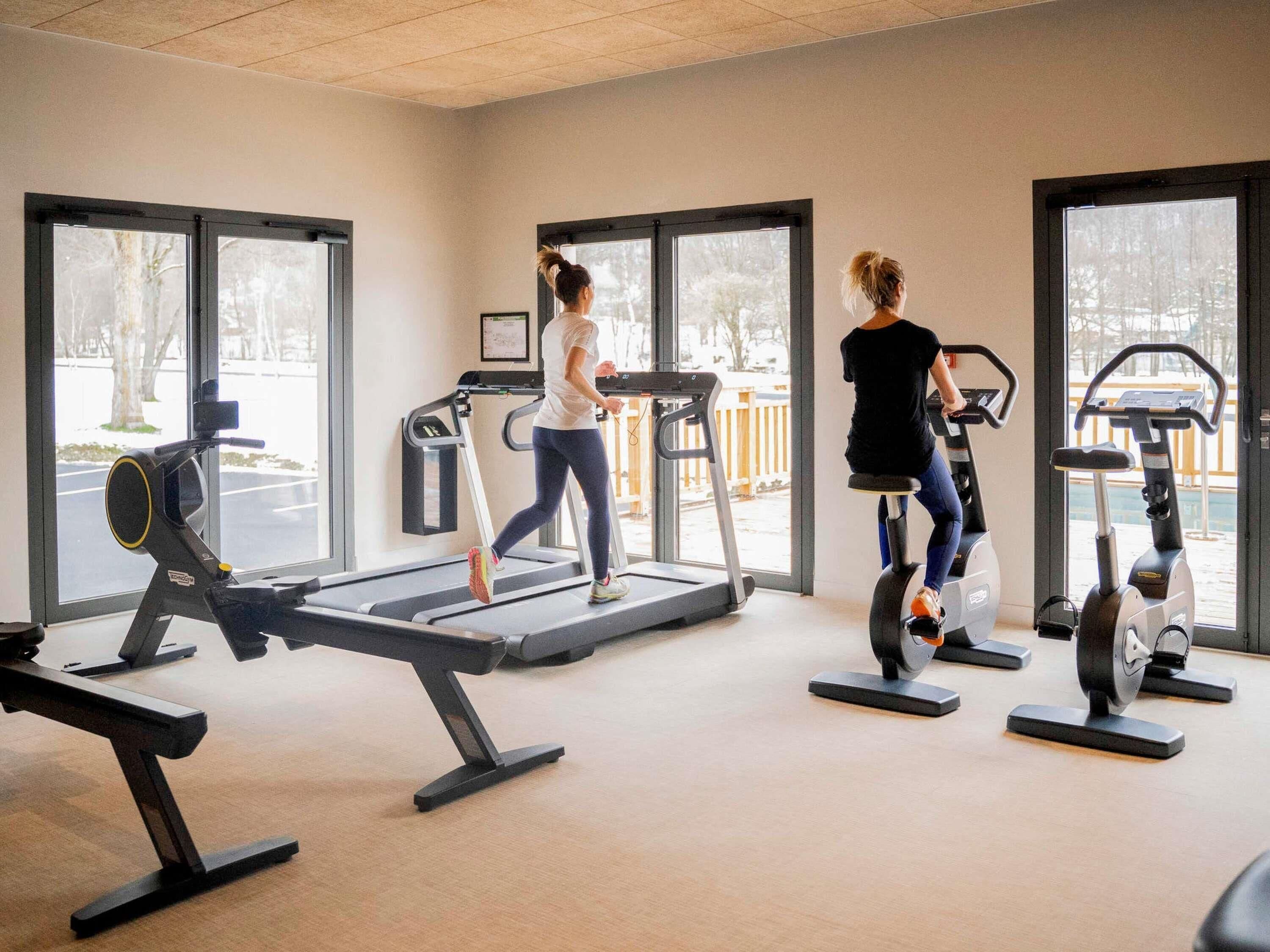 Un gimnasio con cintas de correr y bicicletas estáticas, ventanas amplias y vistas a un paisaje nevado.