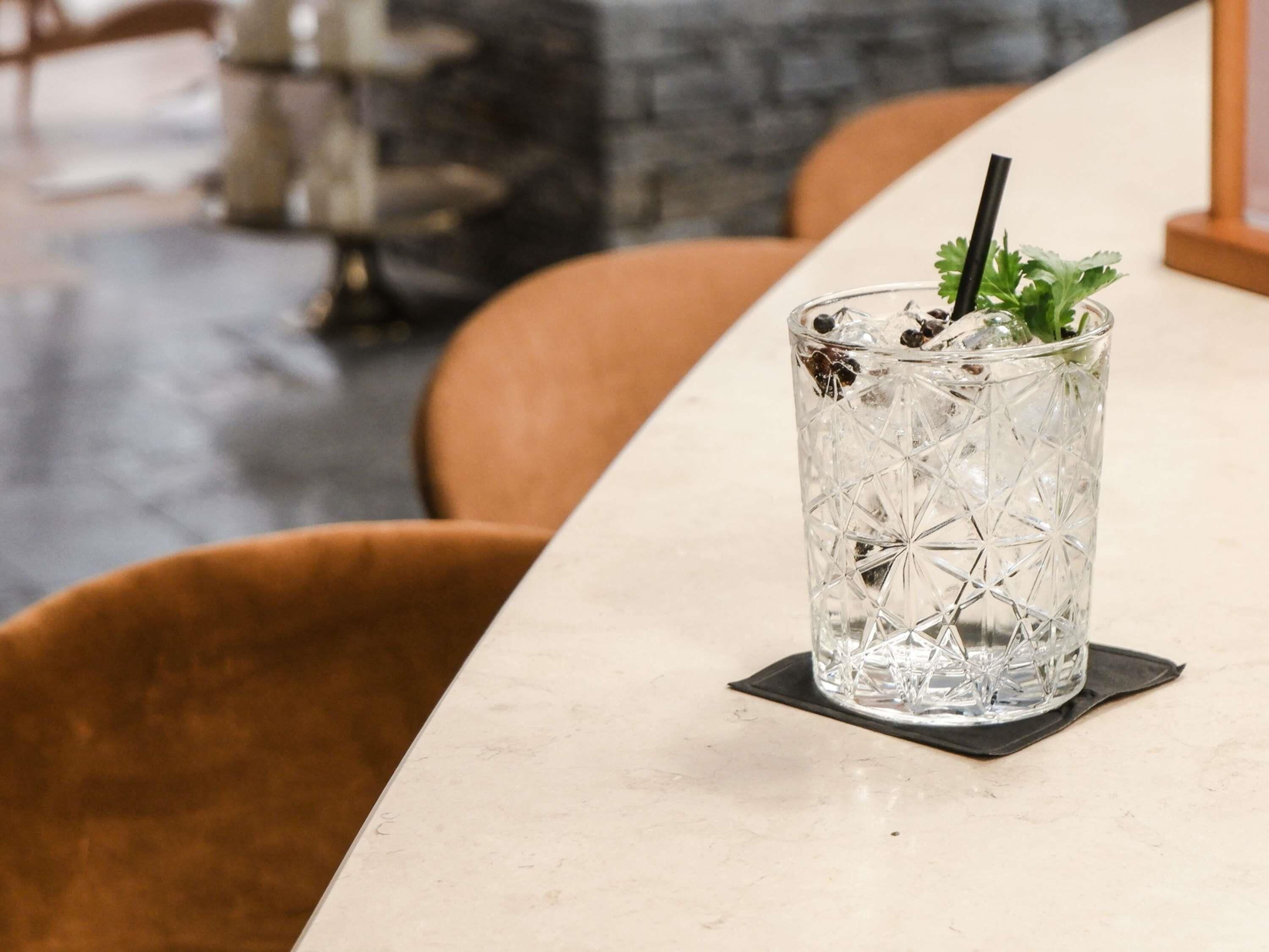 A clear glass with ice cubes, a black straw, and a garnish on a coaster.