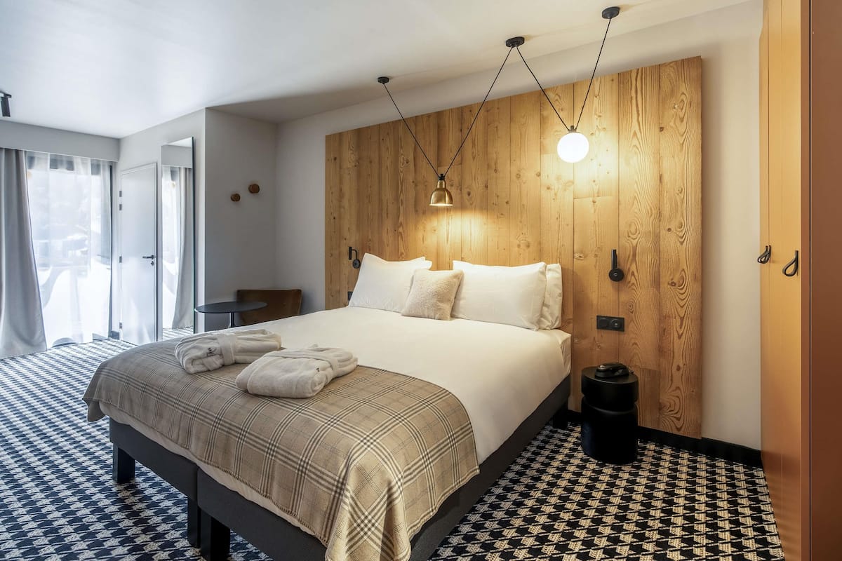 Une chambre d’hôtel avec un lit, un mur décoratif en bois, un luminaire suspendu et un sol à motifs.