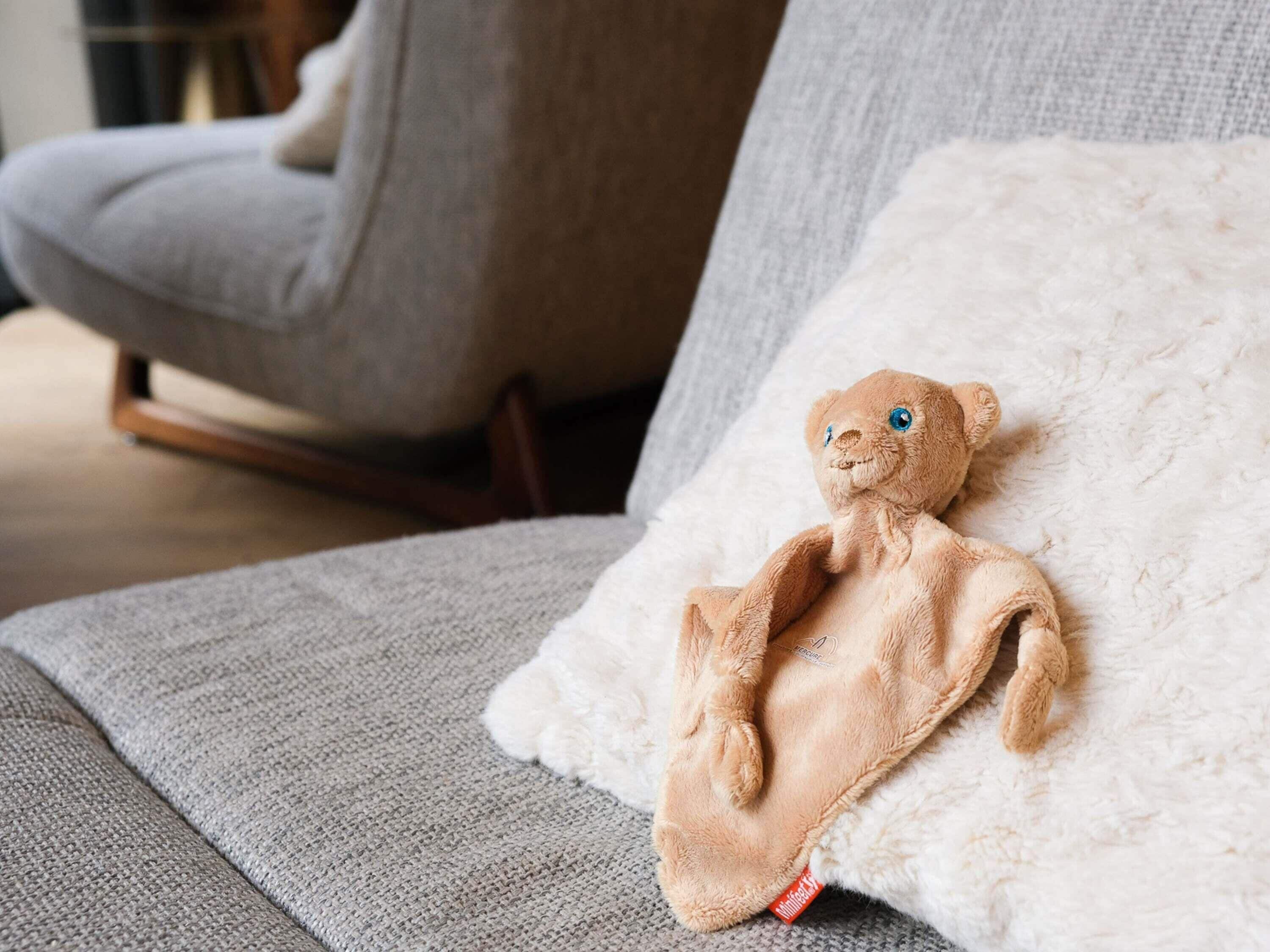 A plush toy on a white fluffy pillow on a grey sofa.