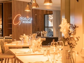 Interior de restaurante con paredes de madera, un letrero de neón, mesas dispuestas con copas de vino y vistas al exterior.