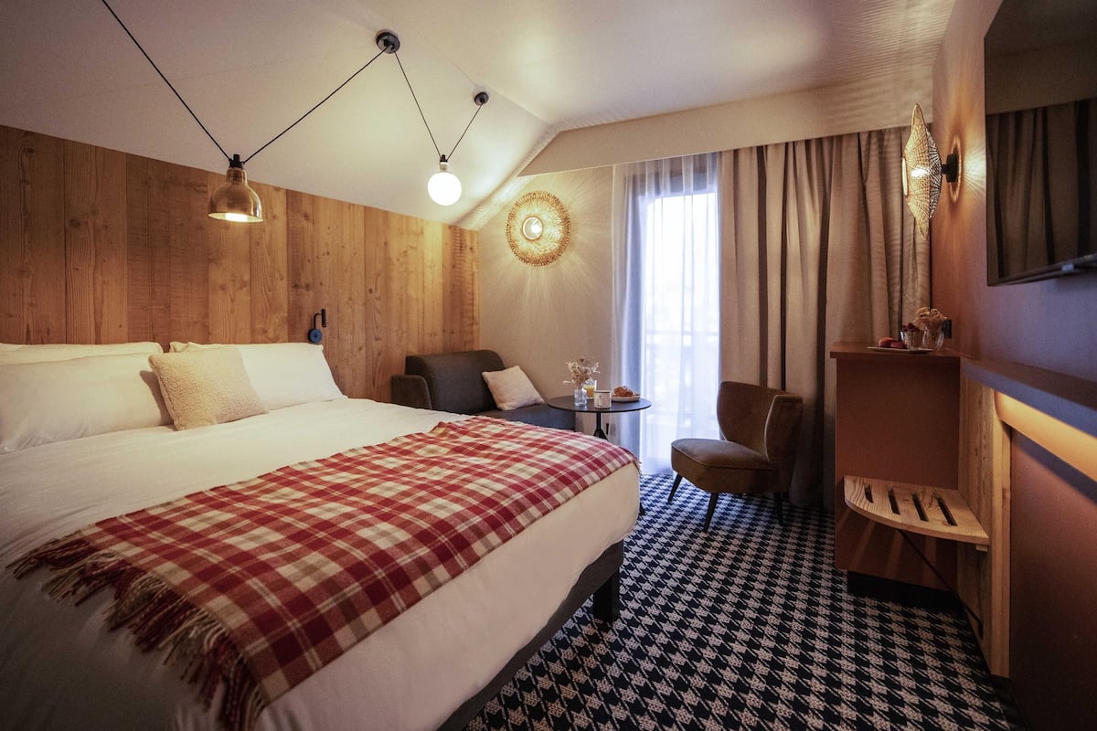 Une chambre d’hôtel avec un grand lit, un bureau, une chaise, une petite table avec une lampe et un téléviseur fixé au mur.