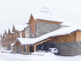 Un edificio cubierto de nieve con fachada de piedra y varios techos puntiagudos, probablemente un hotel o una cabaña.