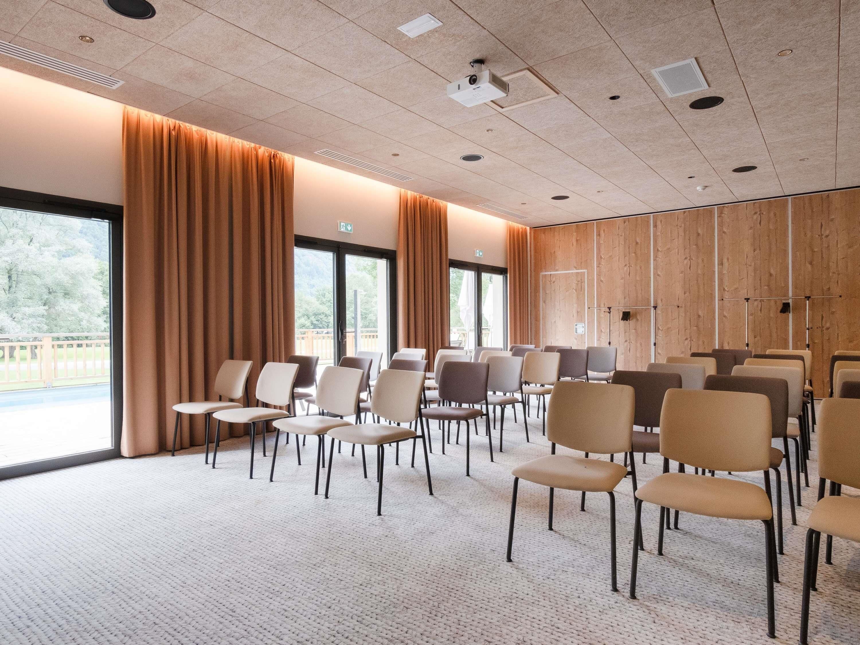 A conference room with rows of chairs, large windows, and a wooden panel wall.