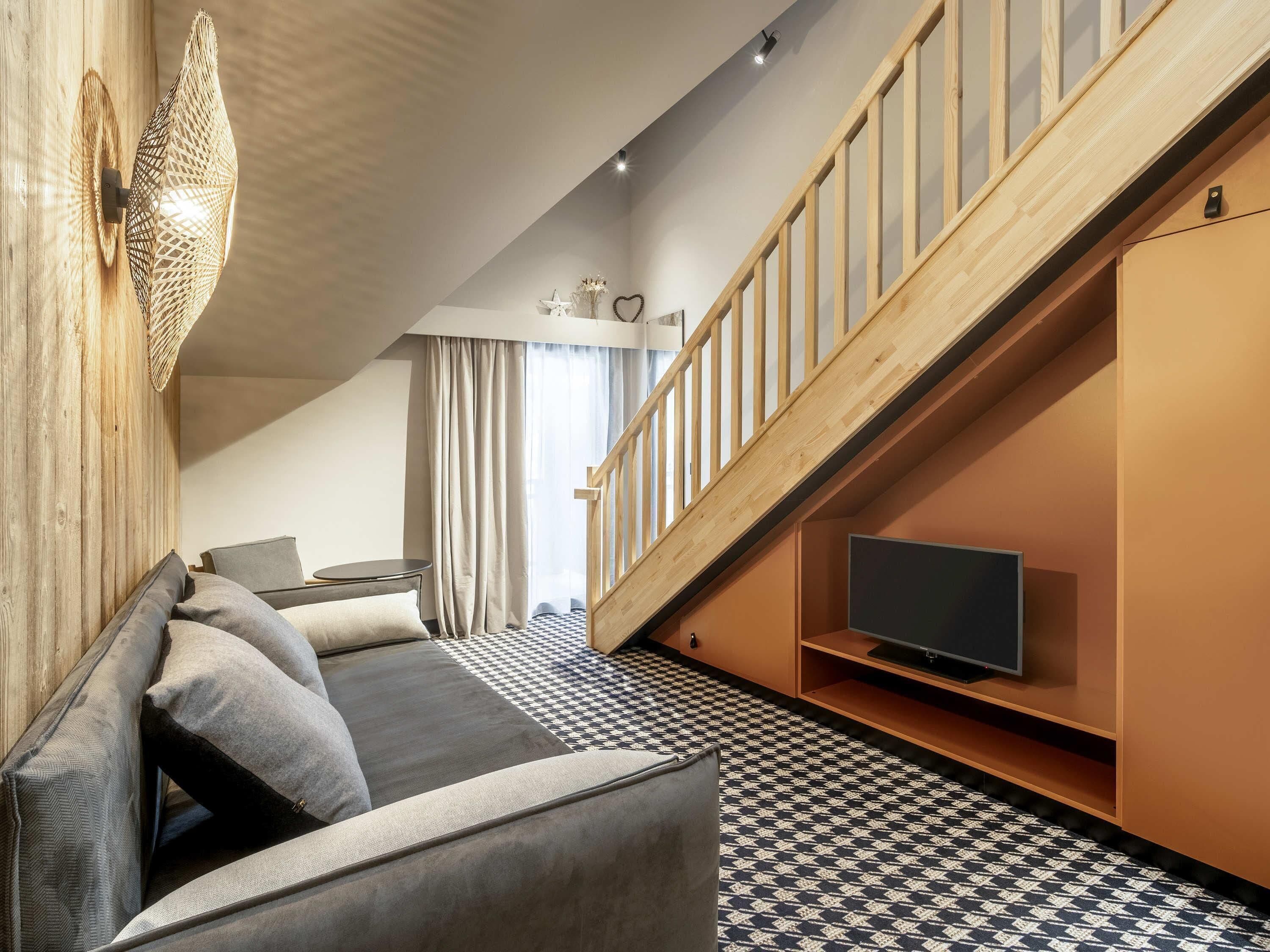 A modern living room with a sofa, television, and a staircase.