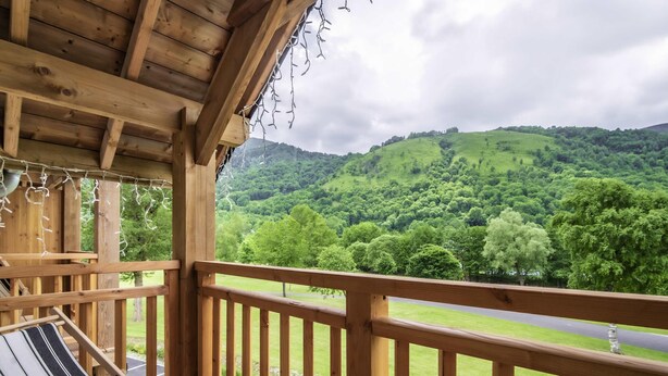 A wooden balcony with a hammock, overlooking a green landscape with trees and hills. - Hôtel Mercure Peyragudes Loudenvielle Pyrénées (Loudenvielle)